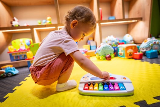 Young child exploring music with a toy piano in a vibrant play area
