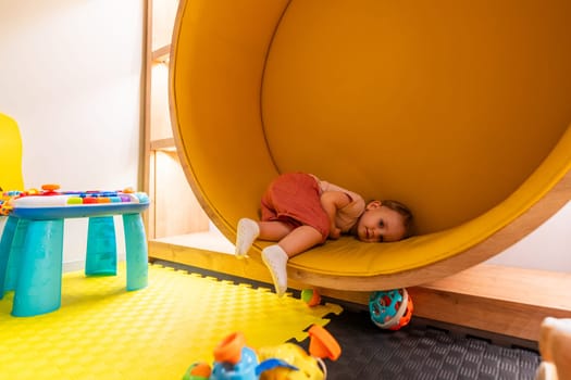 Young child lying down inside a round yellow play nook in a vibrant daycare playroom