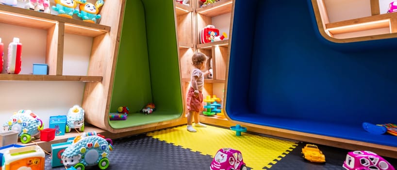 Child playing in a colorful playroom with shelves full of toys and cushioned seating areas