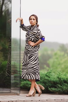 High fashion photo of a beautiful elegant young woman in a pretty zebra print dress posing outdoor. Slim figure.
