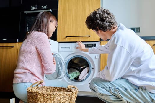 Family mother and teenage son together, at home near the washing machine, lifestyle, adolescence, communication, relationships, everyday domestic routine concept
