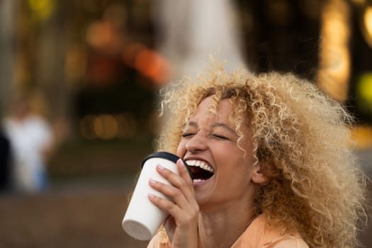 side view headshot of young latin woman with curly hair laughing while taking a coffee.