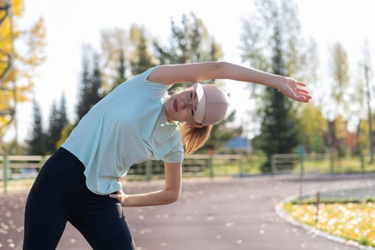 A young beautiful woman in sportswear plays sports at a local stadium. Exercise, jog and exercise at the beginning of the day. Healthy and active lifestyle.