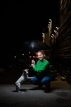 Woman sheltering jack russell terrier dog under umbrella from rain