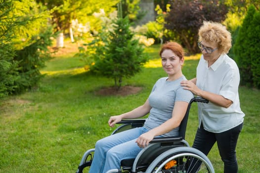An elderly woman is carrying an adult daughter sitting in a wheelchair. Walk outdoors