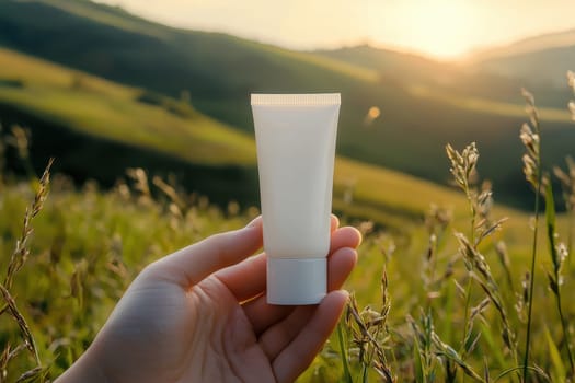 A hand elegantly showcases a white cosmetic tube in a breathtaking natural landscape during sunset, highlighting the product in a serene environment perfect for beauty and wellness themes.