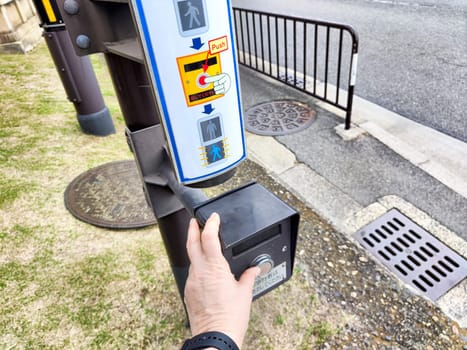 A person presses the button for the pedestrian traffic light at a busy intersection, ready to cross the street safely.