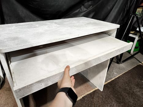 A hand pulls out a drawer from a handmade wooden table, showcasing its practical design and clean lines in a workshop setting.