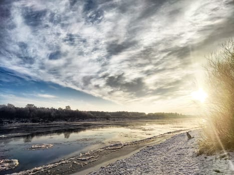 Spring sunlight illuminates the river, showcasing drifting ice and a peaceful shoreline, inviting reflection on the changing seasons.