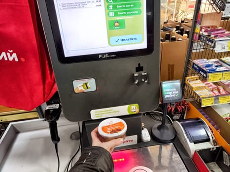 Krasnoyarsk, Russia - November 06, 2024: Customer uses a self-service checkout station in a Krasnoyarsk grocery store, handling a shopping item while making a transaction.