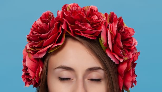 A young girl wearing a vibrant Ukrainian national suit stands against a blue background. She is adorned with a floral headpiece, exuding cultural pride and beauty.