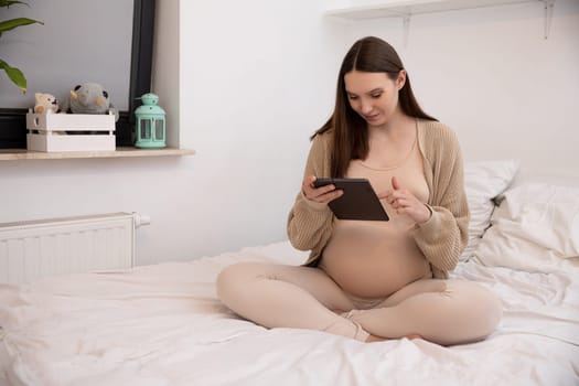 A serene moment captures a pregnant woman interacting with her tablet while in a stylish and cozy bedroom space