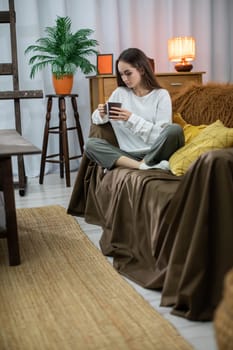 A woman finds joy in sipping coffee within a cozy indoor space that is adorned with vibrant plants and soft textiles