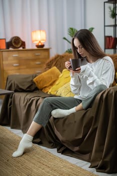 A woman sits back and enjoys a warm cup of coffee in her cozy living room, perfectly embodying comfort and tranquility