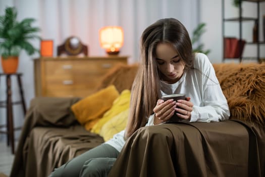 In a warm and inviting living room atmosphere, a young woman intently focuses on her smartphone device