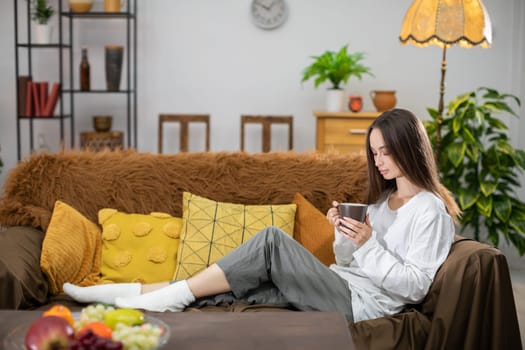 A woman is peacefully relaxing on a couch while enjoying a warm cup of coffee in her stylish, cozy living room