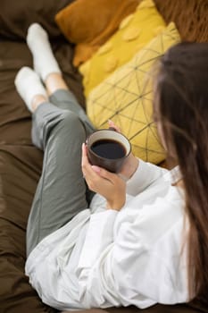 A serene individual finds joy in sipping a warm cup of coffee while relaxing comfortably on a cozy couch