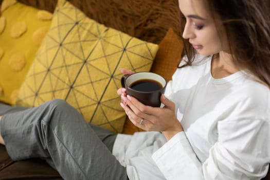 A woman is relaxing peacefully at home, savoring a comforting cup of coffee, radiating tranquility and calmness