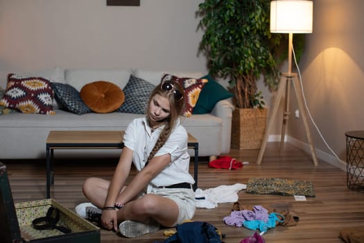 A young individual is diligently sorting through clothes and various belongings in the midst of a messy room