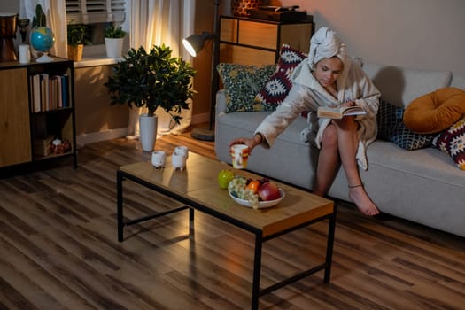 In a cozy living room scene, a woman is happily enjoying delicious snacks while immersed in a captivating book