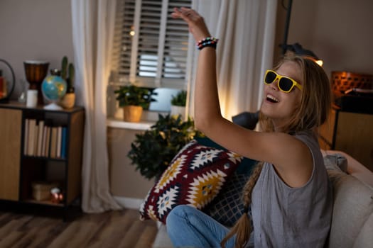 A young woman is having fun dancing to music at home, wearing stylish sunglasses and expressing her joy