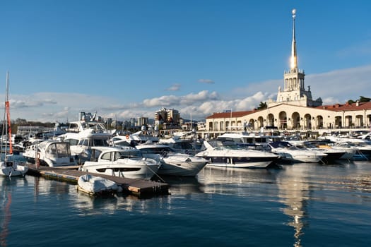 Yachts and boats docked at a marina next to a historic building in a coastal city under a cloudy sky in the late afternoon - Sochi, Russia April 14, 2023.