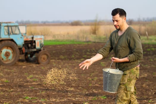 man sowing grain with his hands in a field, people
