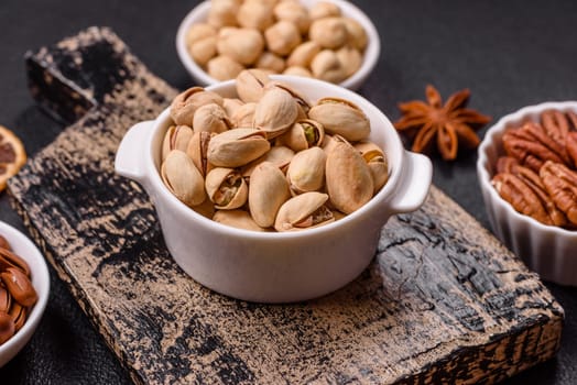 Delicious nutritious pistachio nuts in ceramic bowl on dark concrete background