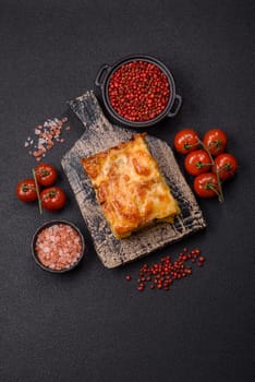 Lasagna or pasta layered with meat, cheese, salt, spices and herbs on dark concrete background