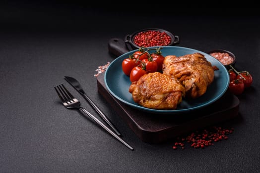 Delicious juicy chicken thighs baked with salt, spices and herbs in a ceramic plate on a dark concrete background