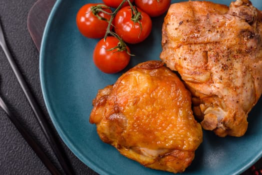 Delicious juicy chicken thighs baked with salt, spices and herbs in a ceramic plate on a dark concrete background