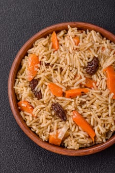Delicious fresh pilaf with rice, carrots, meat, onions, spices and berries on a ceramic plate on a dark concrete background