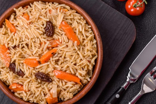 Delicious fresh pilaf with rice, carrots, meat, onions, spices and berries on a ceramic plate on a dark concrete background