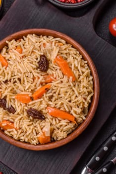 Delicious fresh pilaf with rice, carrots, meat, onions, spices and berries on a ceramic plate on a dark concrete background