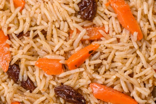 Delicious fresh pilaf with rice, carrots, meat, onions, spices and berries on a ceramic plate on a dark concrete background