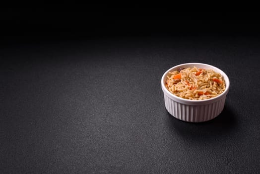 Delicious fresh pilaf with rice, carrots, meat, onions, spices and berries on a ceramic plate on a dark concrete background