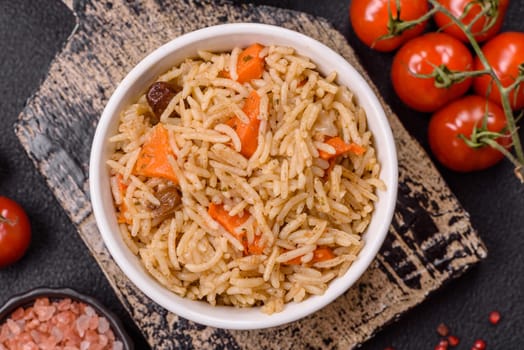 Delicious fresh pilaf with rice, carrots, meat, onions, spices and berries on a ceramic plate on a dark concrete background