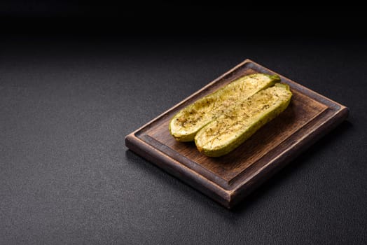 Delicious zucchini cut into two halves baked with salt, spices and herbs on a dark concrete background