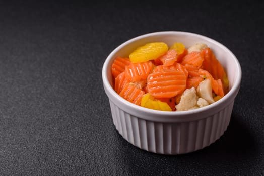 Delicious fresh vegetables steamed carrots, broccoli, cauliflower on a black plate on a dark concrete background