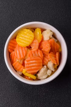 Delicious fresh vegetables steamed carrots, broccoli, cauliflower on a black plate on a dark concrete background