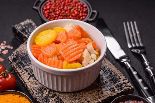 Delicious fresh vegetables steamed carrots, broccoli, cauliflower on a black plate on a dark concrete background