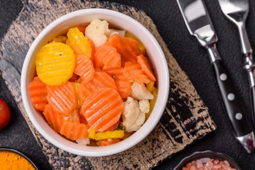 Delicious fresh vegetables steamed carrots, broccoli, cauliflower on a black plate on a dark concrete background