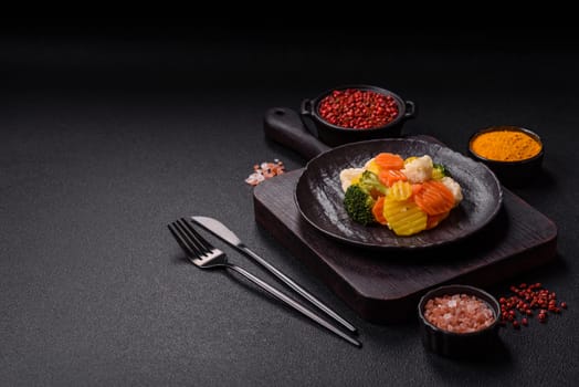 Delicious fresh vegetables steamed carrots, broccoli, cauliflower on a black plate on a dark concrete background