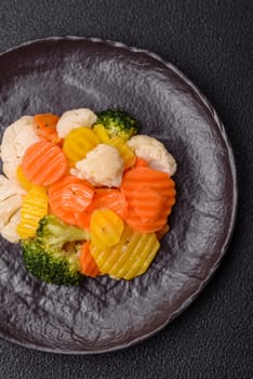 Delicious fresh vegetables steamed carrots, broccoli, cauliflower on a black plate on a dark concrete background