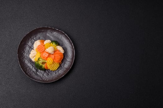 Delicious fresh vegetables steamed carrots, broccoli, cauliflower on a black plate on a dark concrete background