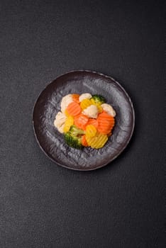 Delicious fresh vegetables steamed carrots, broccoli, cauliflower on a black plate on a dark concrete background