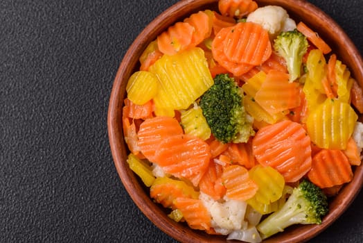 Delicious fresh vegetables steamed carrots, broccoli, cauliflower on a black plate on a dark concrete background