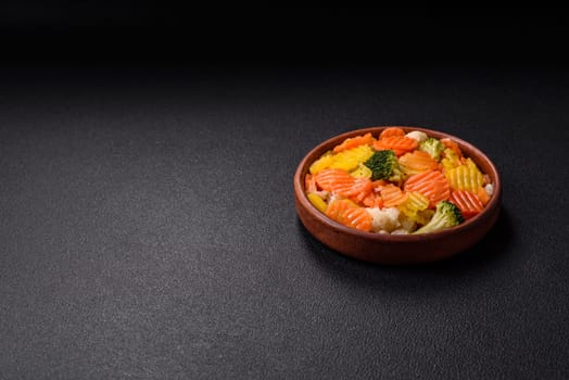 Delicious fresh vegetables steamed carrots, broccoli, cauliflower on a black plate on a dark concrete background