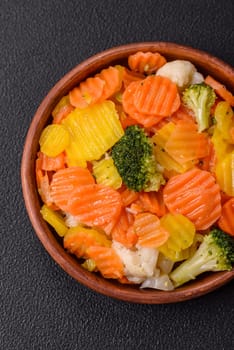 Delicious fresh vegetables steamed carrots, broccoli, cauliflower on a black plate on a dark concrete background
