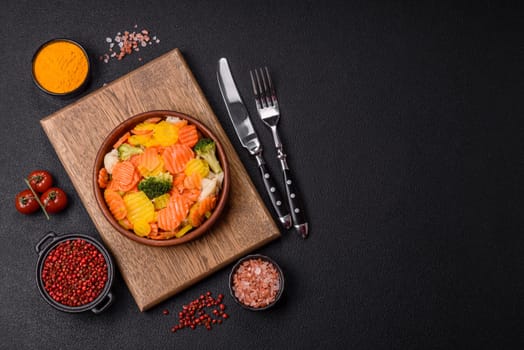 Delicious fresh vegetables steamed carrots, broccoli, cauliflower on a black plate on a dark concrete background